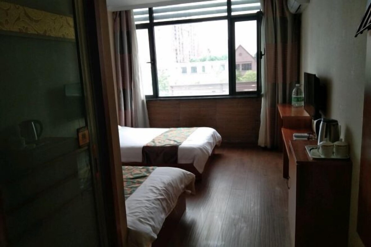 Una habitación de hotel con dos camas, un escritorio de madera con televisor y una ventana con cortinas.