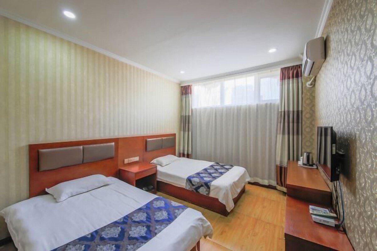 Habitación de hotel con dos camas, cabecera de madera, mesita de noche, televisor y ventana con cortinas.