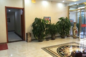 Un vestíbulo con suelo de mármol, plantas en macetas y una alfombra estampada.