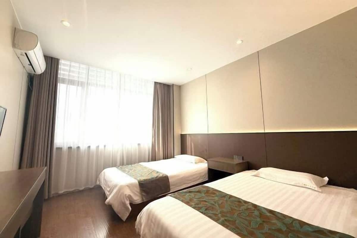 A hotel room with two beds, a desk, a chair, a TV, and a window with curtains.