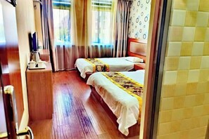 Una habitación de hotel con dos camas, suelo de madera, una mesita con cafetera y cortinas.