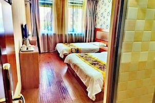 Una habitación de hotel con dos camas, suelo de madera, una mesita con cafetera y cortinas.