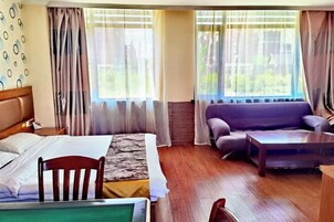 Una habitación de hotel con cama, una silla de madera, un sofá, una mesita de centro y ventanas grandes con cortinas.