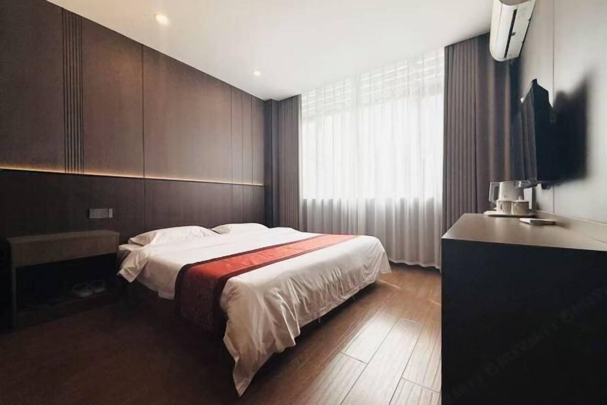 A modern hotel room with a large bed, a bedside table, a flat-screen TV, and a window with curtains.