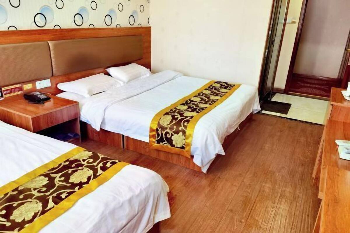 A hotel room with two beds, wooden headboards, a bedside table with a phone, and a patterned bed runner.