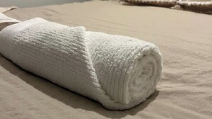 A neatly rolled white towel on a bed with a textured beige cover. - Views from the 8th (London)