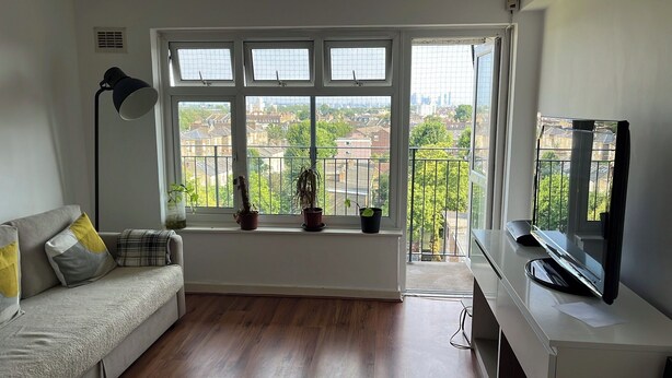 A living room with a sofa, a TV, and a window with a view of buildings and trees. - Views from the 8th (London)