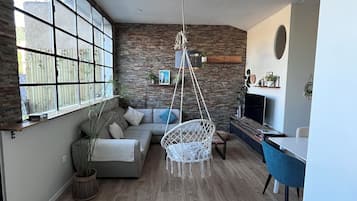 Een moderne woonkamer met een groot raam, een hangstoel, een bank en een eethoek.