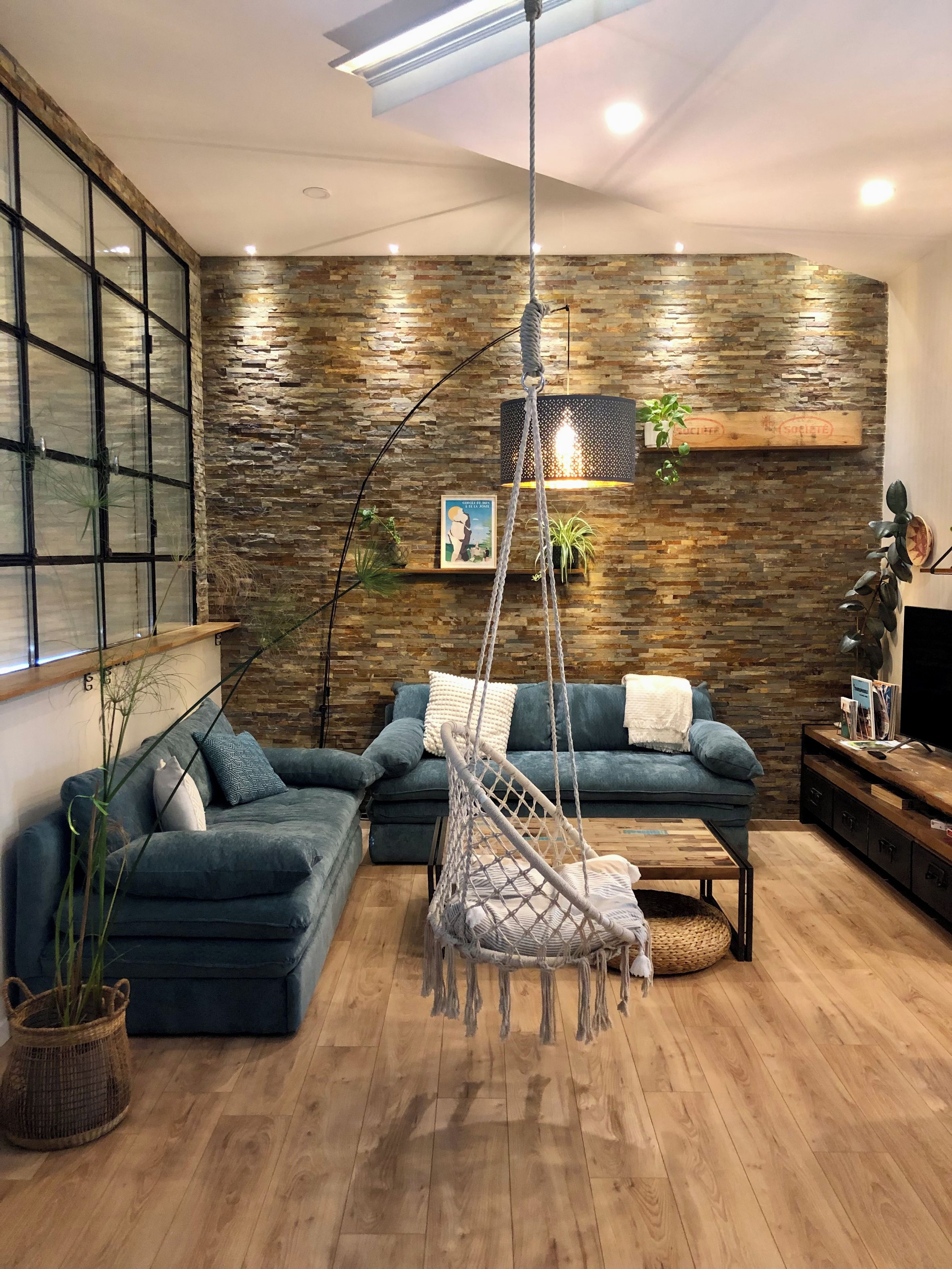 Una sala moderna con un sofá seccional, un sillón colgante y piso de madera.