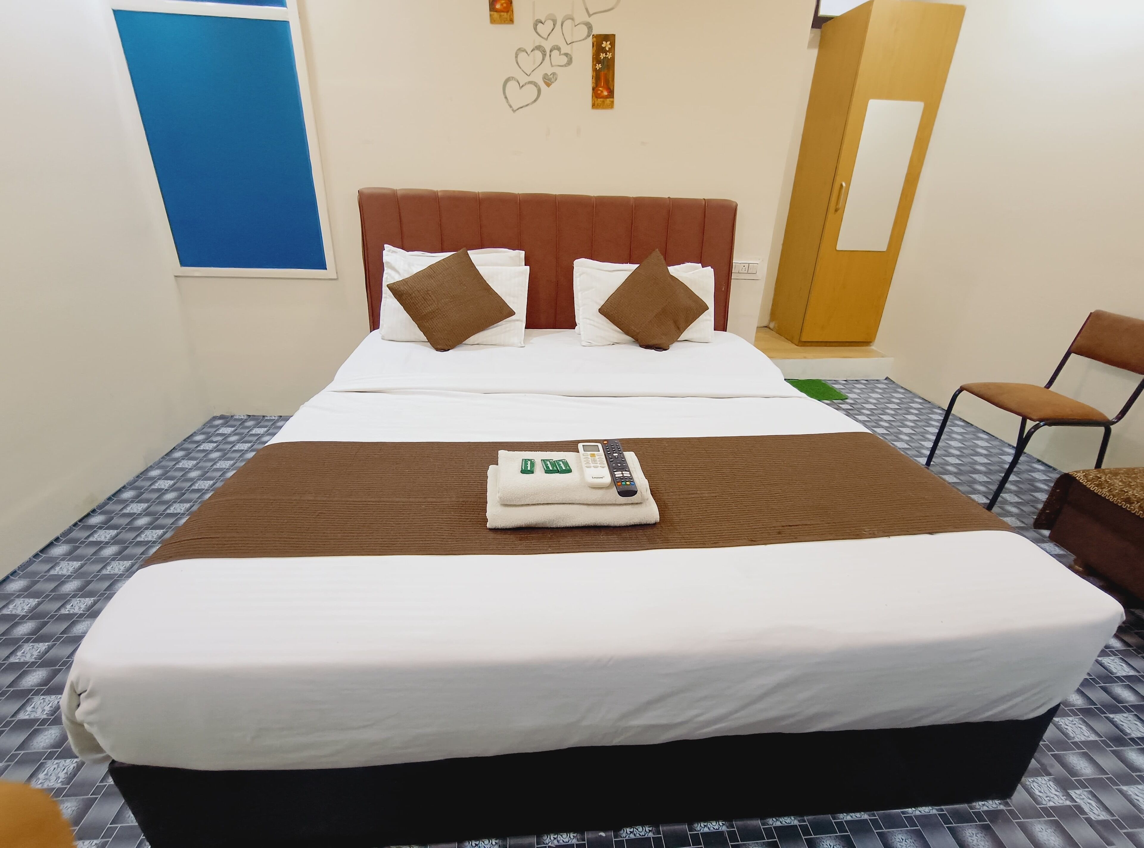 Una cama bien hecha con cabecera marrón, ropa de cama blanca y un control remoto sobre una toalla.