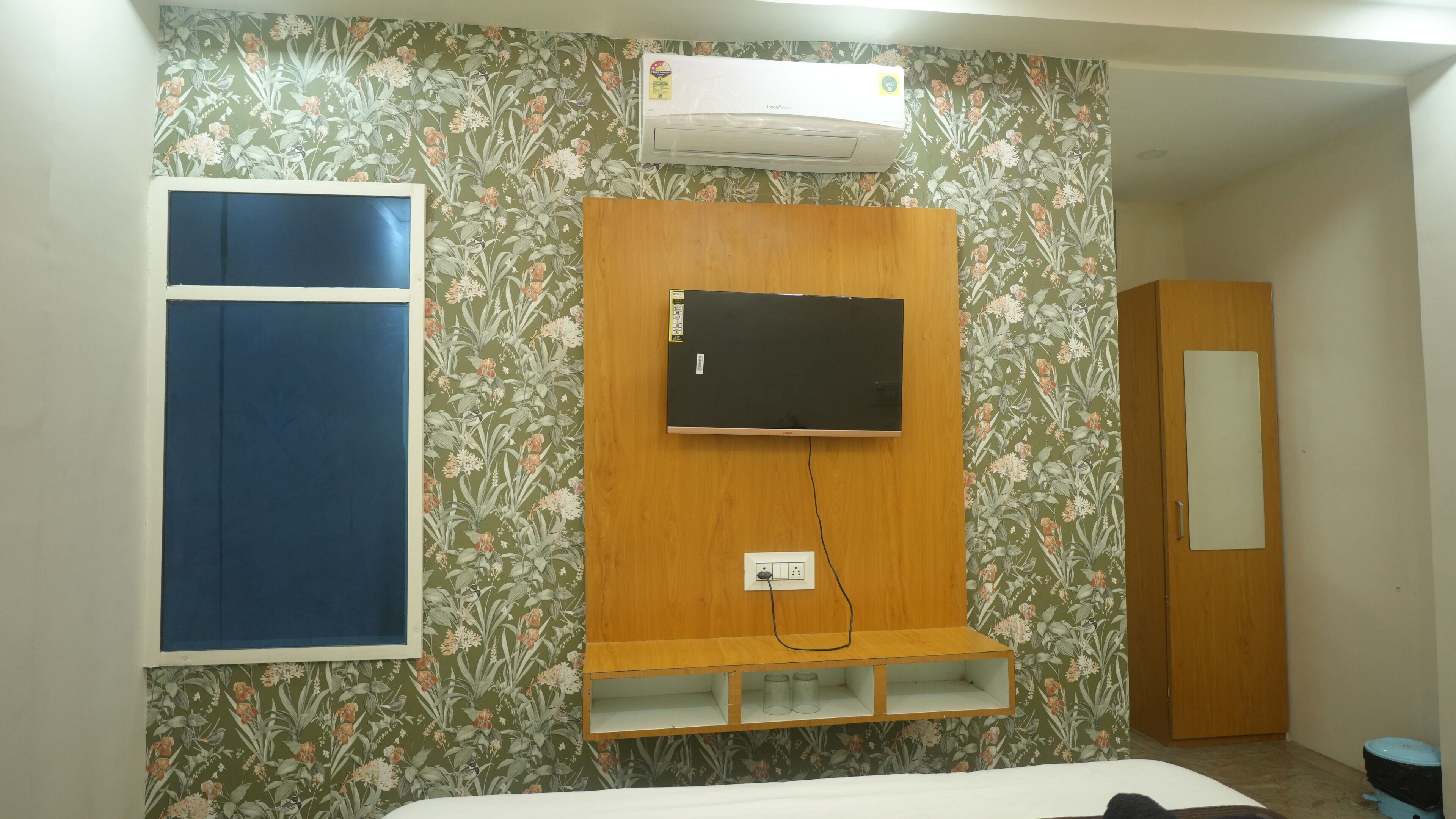 A bedroom with a bed, a mounted TV, a wardrobe, and an air conditioning unit.