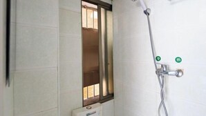 Ein Badezimmer mit weißen Fliesen, einer Dusche inklusive Handbrause und einem Fenster mit Metallrahmen.
