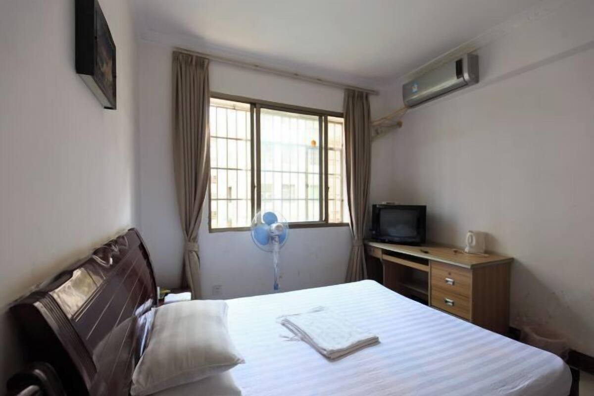 Une chambre d’hôtel équipée d’un lit, d’un bureau avec une télévision, d’une fenêtre avec des rideaux et d’un appareil de climatisation.