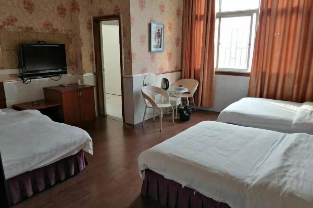 Une chambre d’hôtel avec deux lits, une télévision, un bureau avec une chaise et une fenêtre avec des rideaux.