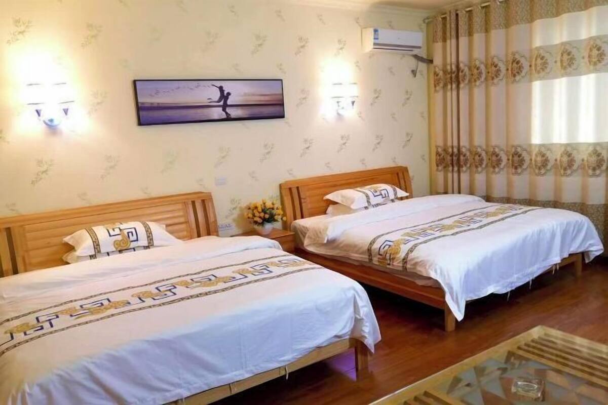 Habitación de hotel con dos camas de madera, una mesita pequeña y aire acondicionado instalado en la pared.