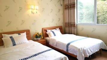 A hotel room with two beds, a nightstand with a vase of flowers, and a window with curtains.