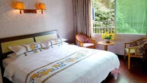 Ein Hotelzimmer mit einem großen Bett, zwei Wandlampen, einem kleinen Tisch mit Blumenvase und einem Sessel.