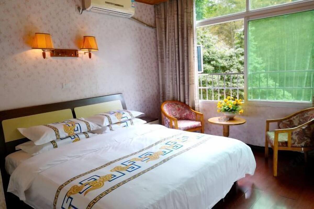 Habitación de hotel con una cama grande, dos lámparas de pared, una mesita con un jarrón de flores y una silla.
