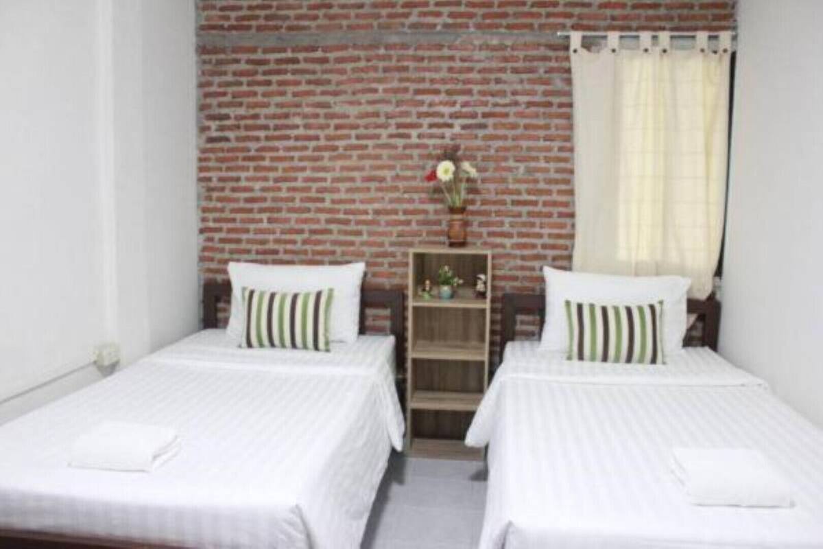 A room with two beds, each with a white bedspread and striped pillows. A wooden shelf with a vase of flowers is between the beds.