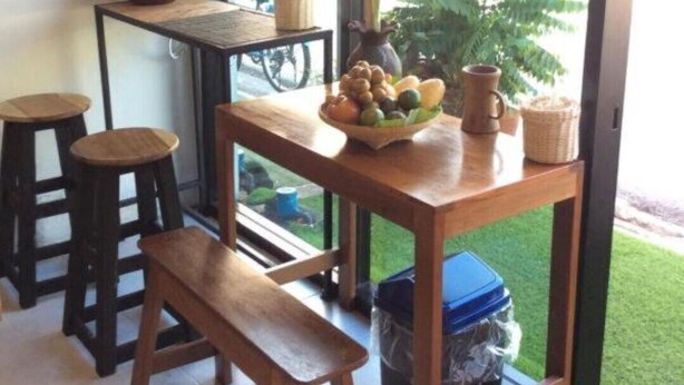 A small, cozy café with a wooden table, stools, and a bench. There are flowers in a vase and a bowl of fruit on the table. - Banana Hostel Donmuang (Bangkok)