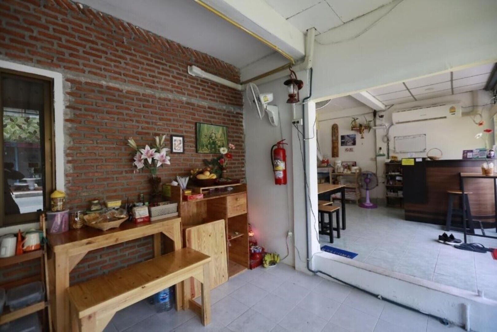 Quarto com parede de tijolos, mobiliário de madeira, um extintor de incêndio e uma área de cozinha com frigorífico e pia.