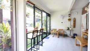 A room with a large window, a wooden table, and chairs. - Banana Hostel Donmuang (Bangkok)
