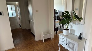 Une pièce spacieuse dotée d’un parquet en bois à motifs chevrons, d’une console blanche avec des tiroirs, d’un grand miroir et d’une plante en pot.