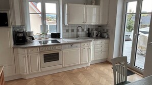 Une cuisine avec des meubles blancs, un four encastré, un évier et une fenêtre donnant sur un quartier résidentiel.