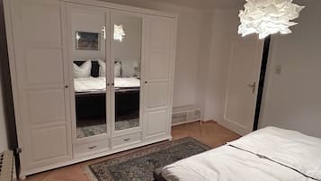Un dormitorio con un armario blanco grande, una cama con ropa de cama blanca y una alfombra estampada.