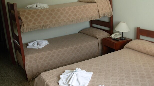 Una habitación de hotel con dos literas, una mesita de noche con lámpara y una cama bien hecha con toallas.