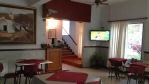 Un comedor con mesas y sillas, una escalera, un televisor y un cuadro en la pared.
