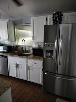 A modern kitchen with stainless steel appliances, white cabinetry, and a granite countertop. - 3-bedroom home with AC refrigeration unit, WiFi, garage plus carport. 100% tile (El Paso)