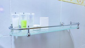 A bathroom with a glass shelf holding toiletries, a shower curtain rod, and a towel rack. - Markson Hotel Kilimani (Nairobi)