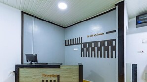 A reception desk with a wooden finish and a sign that reads "Reception." The wall behind features a design with vertical and horizontal lines. - Markson Hotel Kilimani (Nairobi)