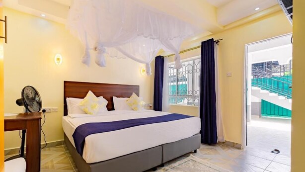 A bedroom with a bed, bedside table, and a fan. - Markson Hotel Kilimani (Nairobi)
