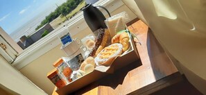 Bandeja de desayuno con pastelería y una cafetera en un balcón con vistas al mar.