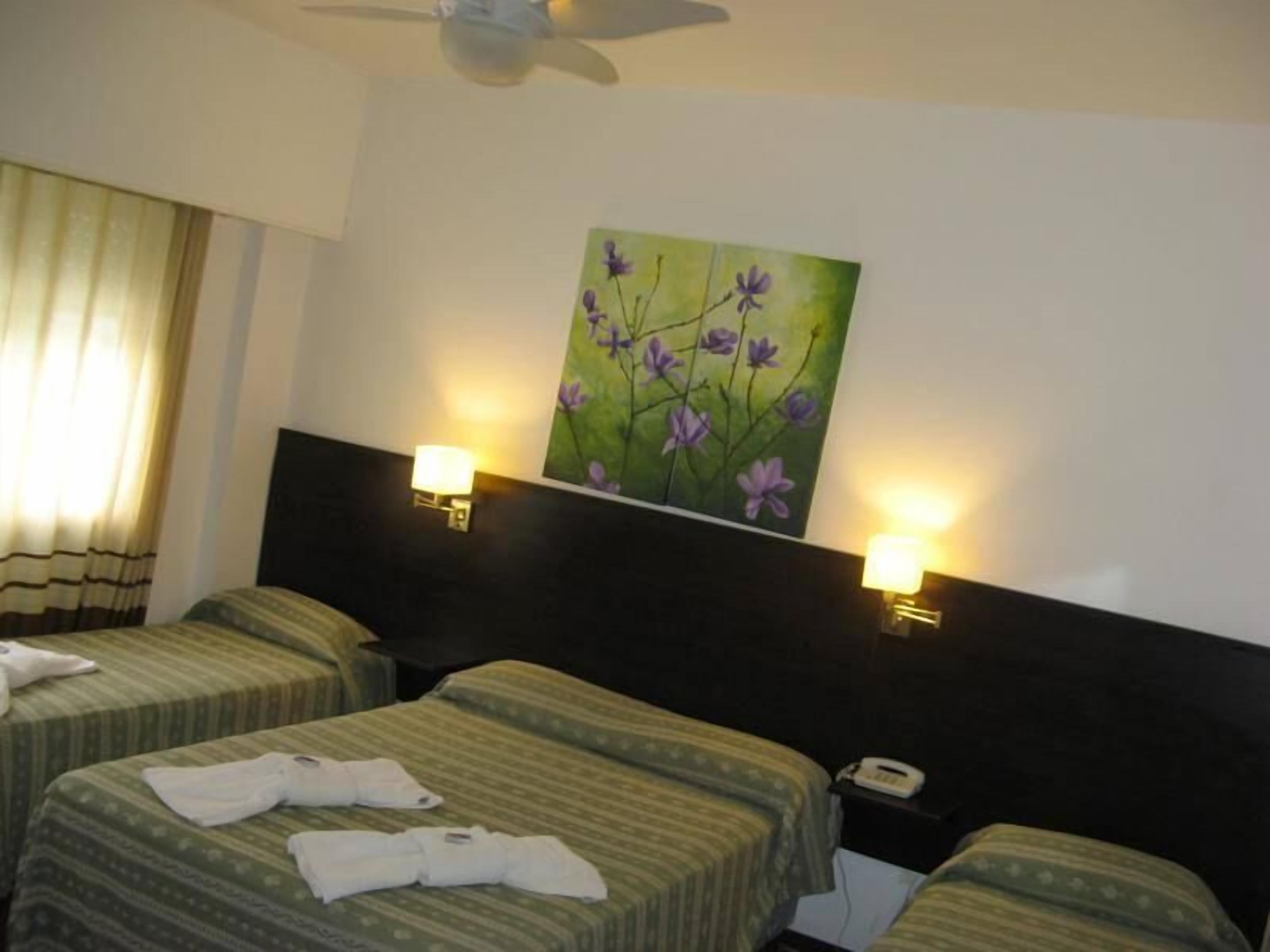 A hotel room with two beds, a painting of purple flowers on the wall, and two bedside lamps.