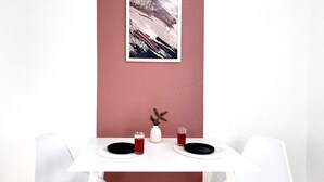 Una mesa de comedor con dos sillas, un florero con plantas secas y dos vasos de bebida roja.