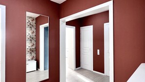 Un pasillo con paredes rojas, puertas blancas y un espejo que refleja un baño con papel tapiz floral.