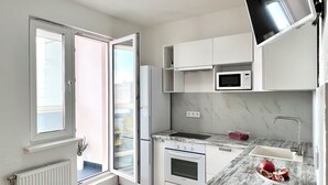 Una cocina moderna con armarios blancos, microondas integrado, pileta de acero inoxidable y una planta en maceta.
