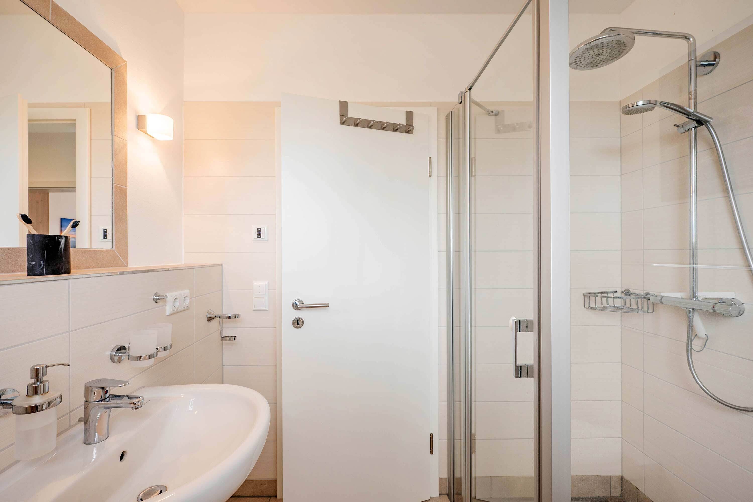 Ein modernes Badezimmer mit einer Duschkabine, einem weißen Waschbecken und einem Spiegel.