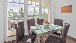 Uma sala de jantar com mesa, cadeiras e vista através de grandes janelas.