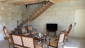 Un salon avec un escalier en bois, un téléviseur et une table basse avec des fauteuils.
