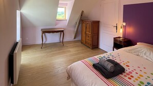 Une chambre avec un plafond en pente, un plancher en bois, un lit recouvert d’une couette à pois colorés, une table de chevet avec une lampe, une armoire en bois et une petite table.