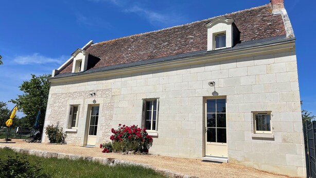 Un bâtiment en pierre avec un toit recouvert de tuiles, deux fenêtres et une porte.