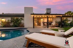 A modern house with a swimming pool, outdoor seating, and string lights.