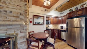 A kitchen with a stone wall, wooden cabinets, a stainless steel refrigerator, and a dining table with chairs.