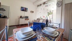 A dining area with a table set for two, a television mounted on the wall, and a decorative wall mural.