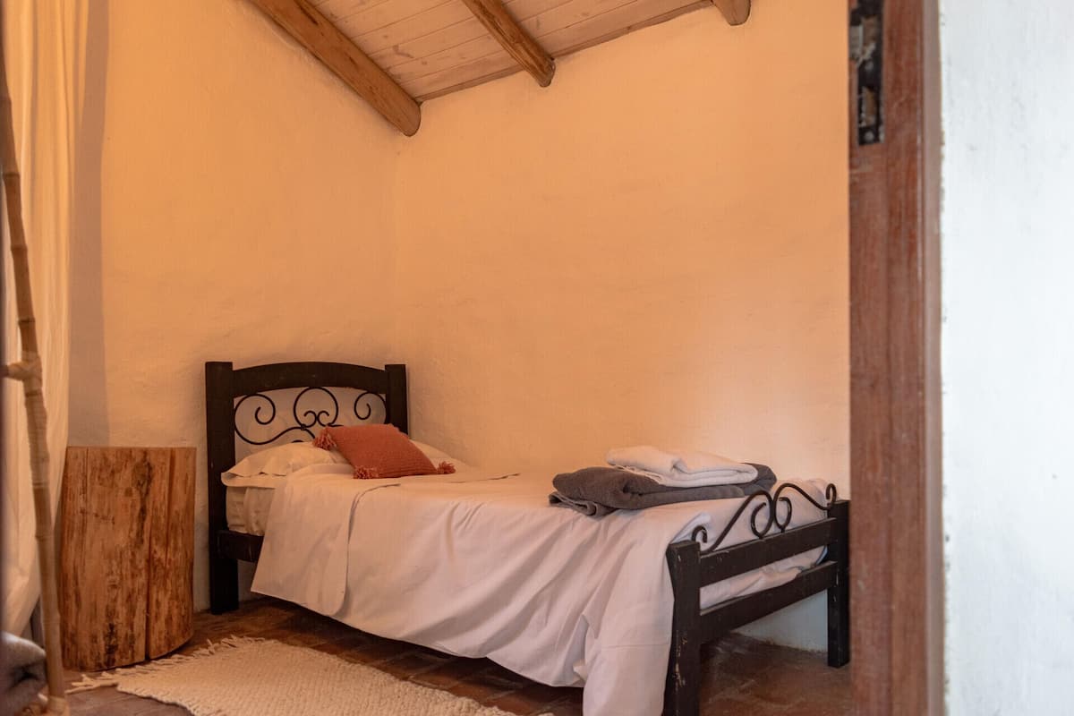 A small, single-bed room with a wooden headboard and a white bedspread.