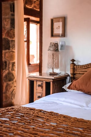 A cozy bedroom with a bed, a nightstand with a lamp, and a stone wall. - Castillo de Piedra Hotel Boutique (Tafi del Valle)